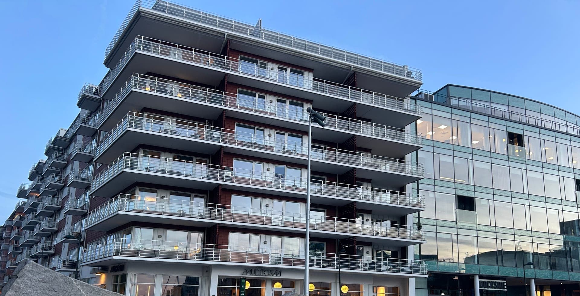 Apartment building with balconies and commercial units at street level, evening light.