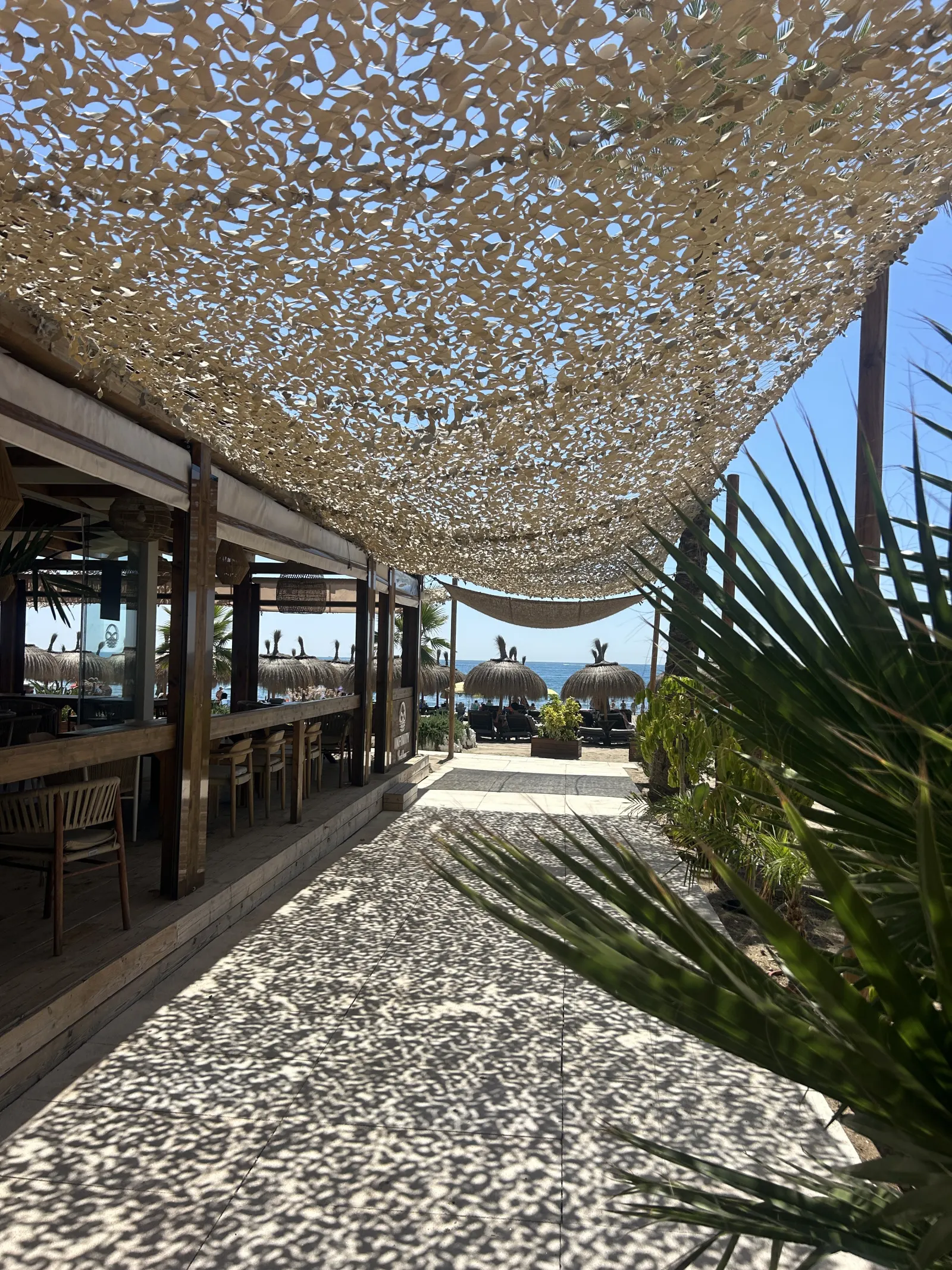 Strandrestaurang under skuggvävnad vid strandpromenaden